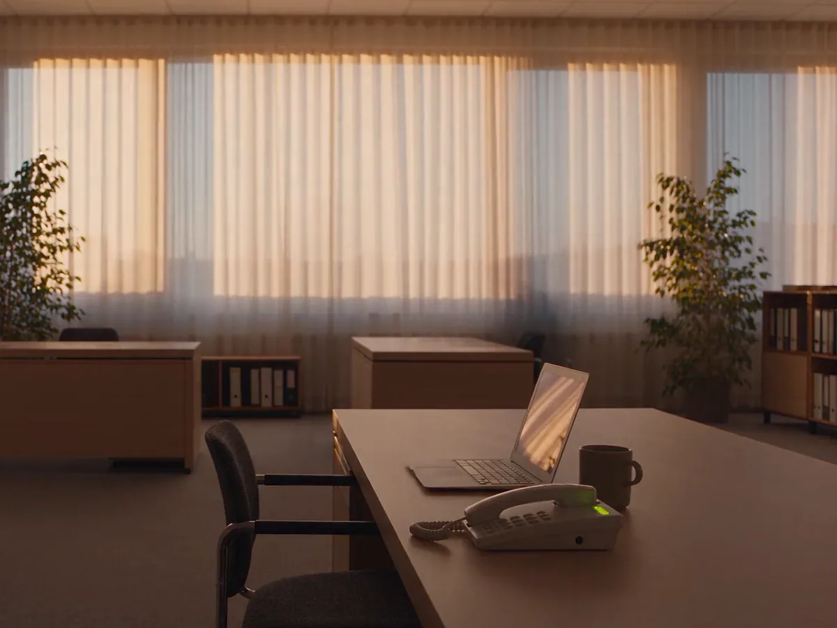 Een stil kantoor in het avondlicht, met een telefoon en een laptop op het bureau