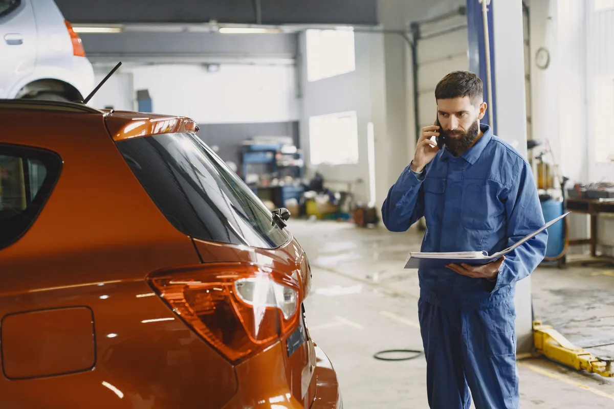 Een monteur neemt in de werkplaats de telefoon op, met een map in zijn hand